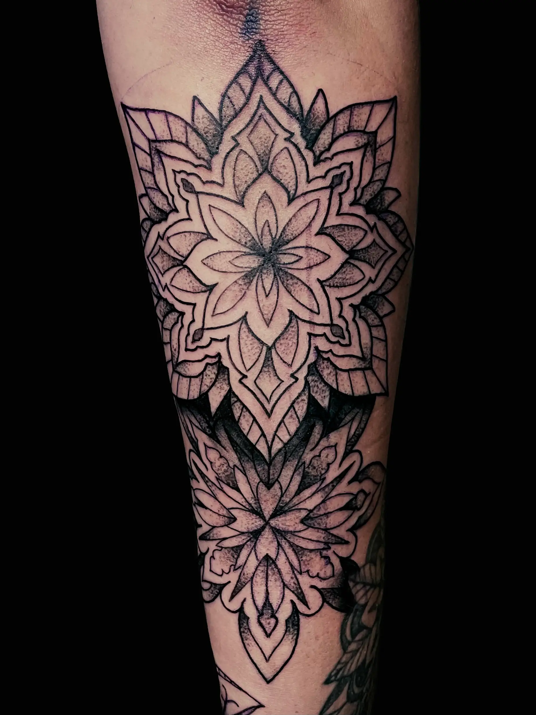 Mandala-style black and grey tattoo with symmetrical floral geometry on lower leg.