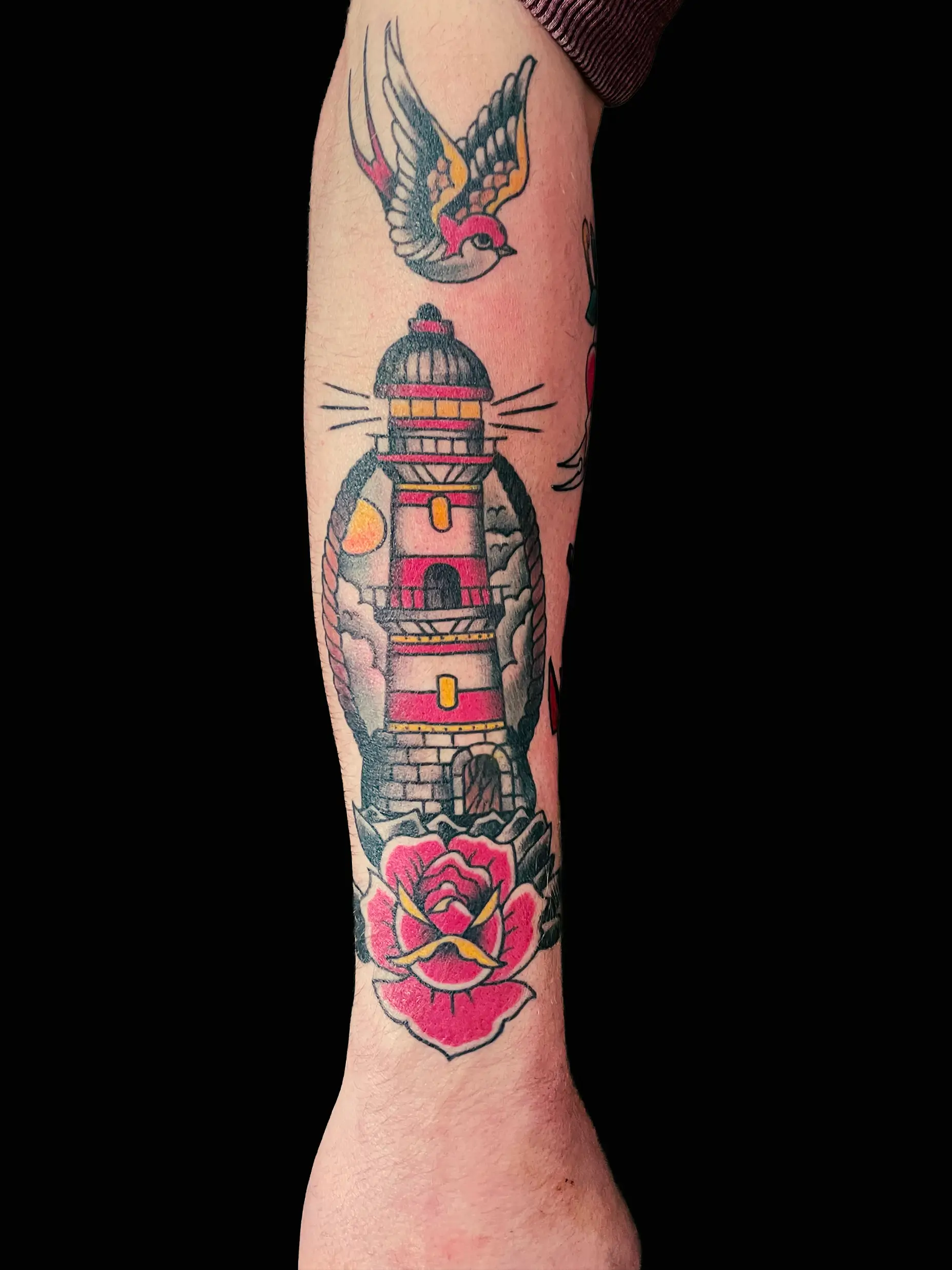 Color tattoo of a lighthouse with a swallow and rose, traditional style with bold outlines on forearm.