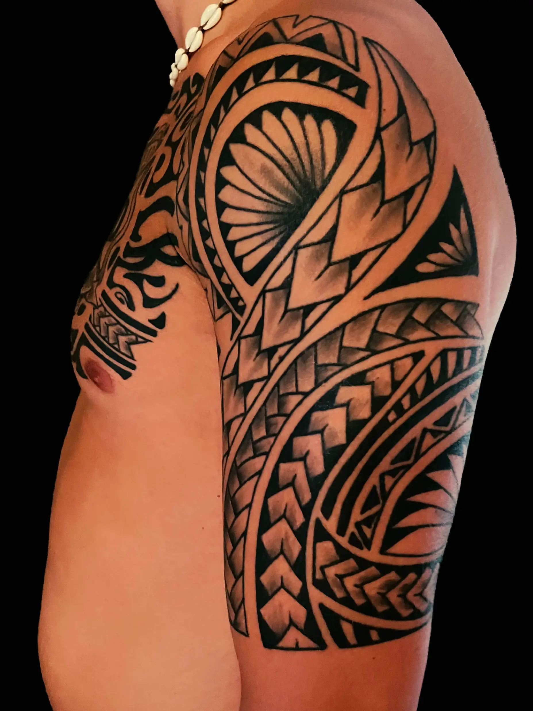 Large Polynesian-style tribal tattoo covering shoulder and upper arm with geometric patterns.