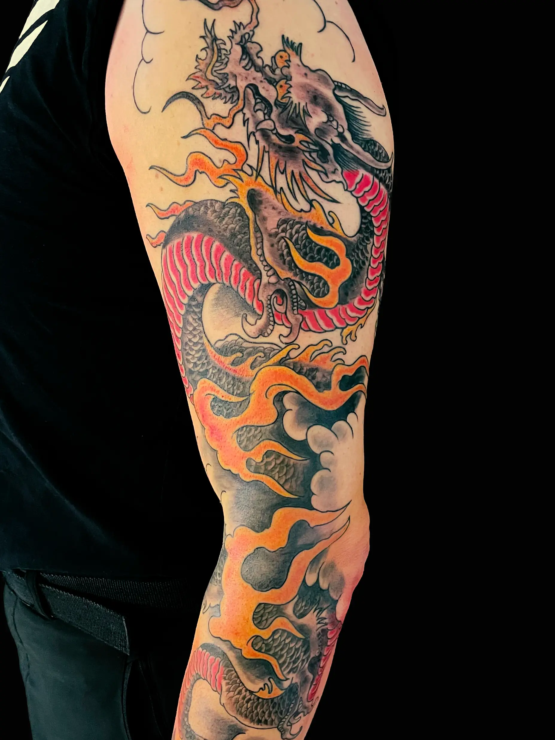 Japanese-style dragon tattoo with flowing flames and clouds, vibrant colors on full arm.