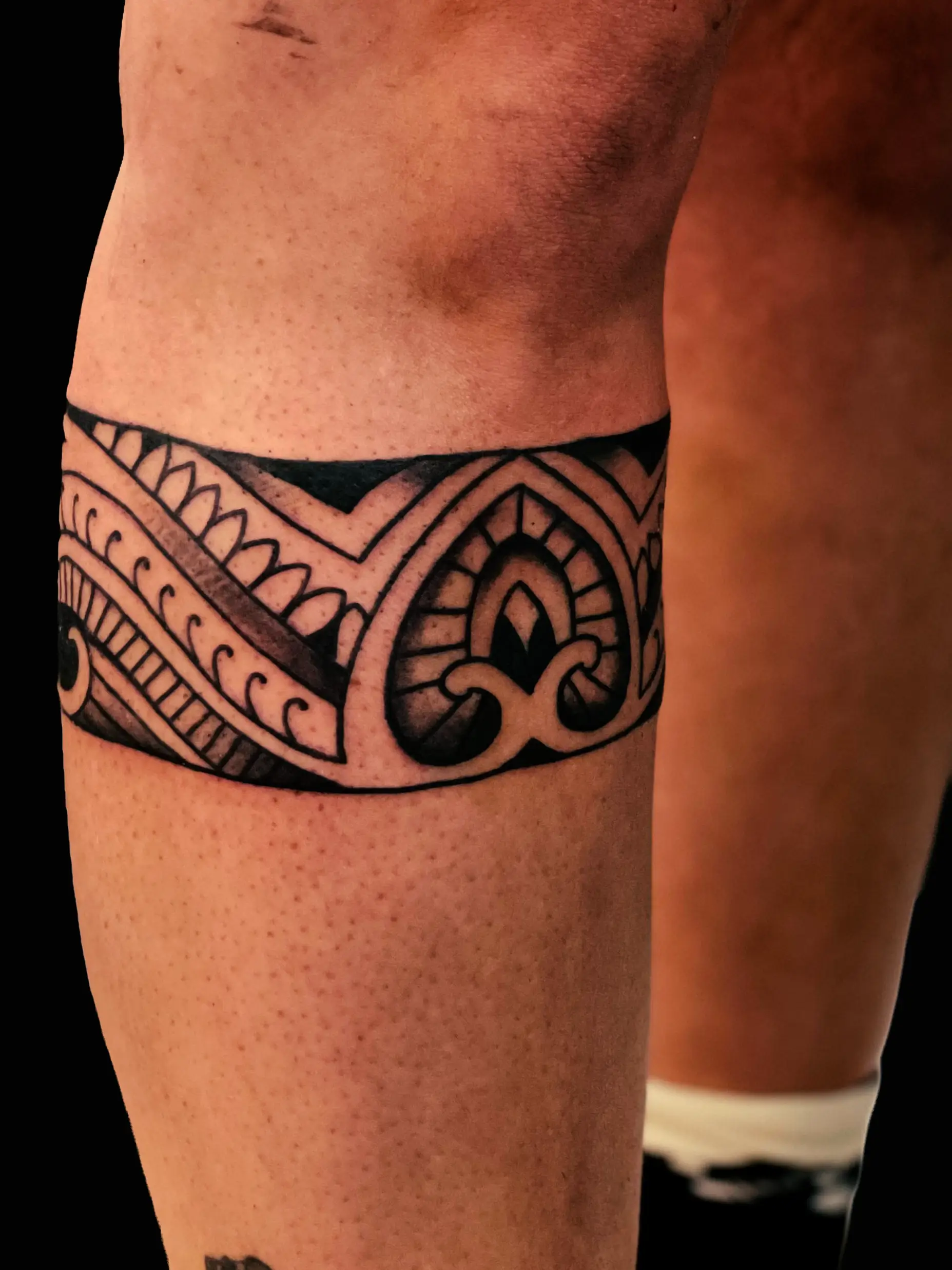 Ornamental band tattoo around upper thigh with geometric and decorative patterns.